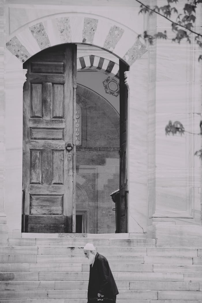 Black and white photo of an elderly man walking past a historic doorway with architectural details.