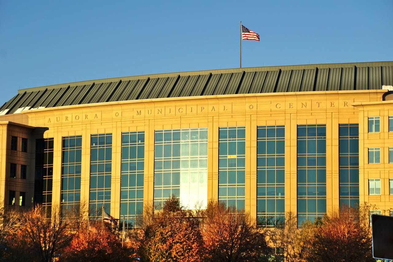 Aurora Municipal Center building with waving American flag in daylight.