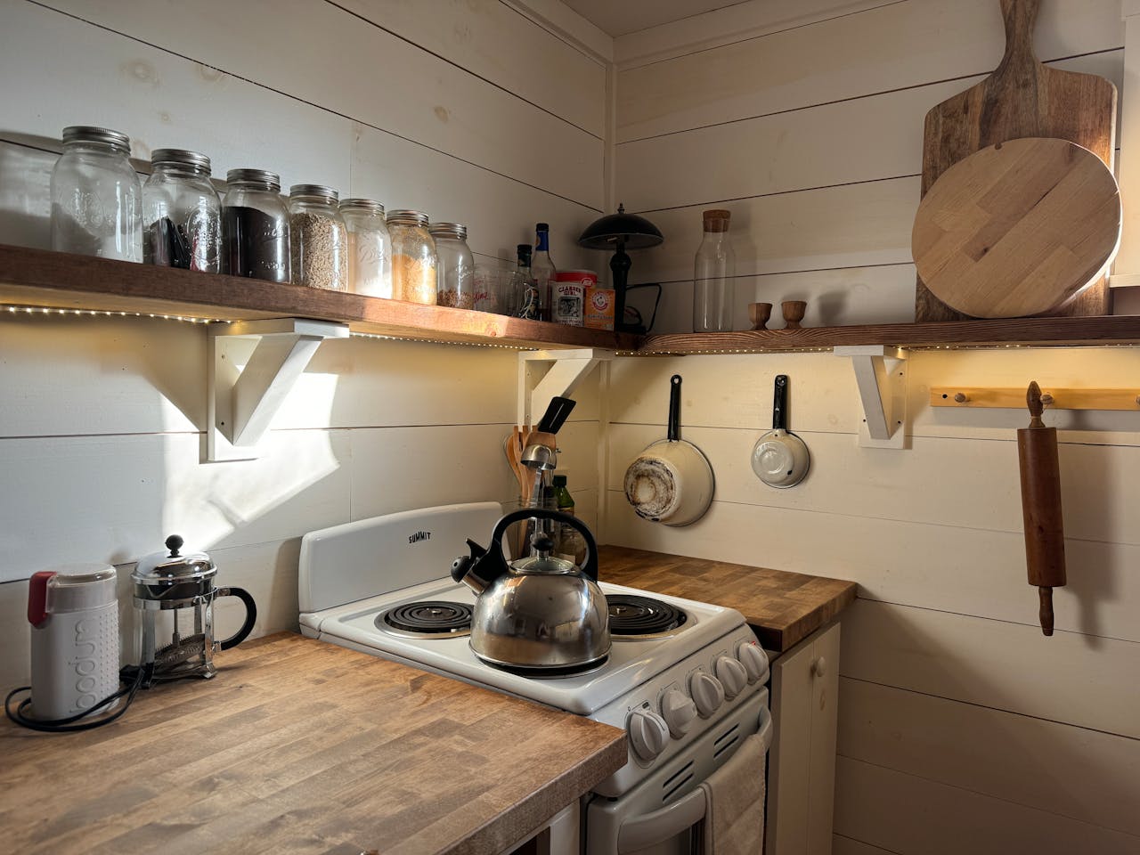 A small rustic kitchen with a wooden shelf, stove, and cooking utensils, offering a warm and cozy atmosphere.